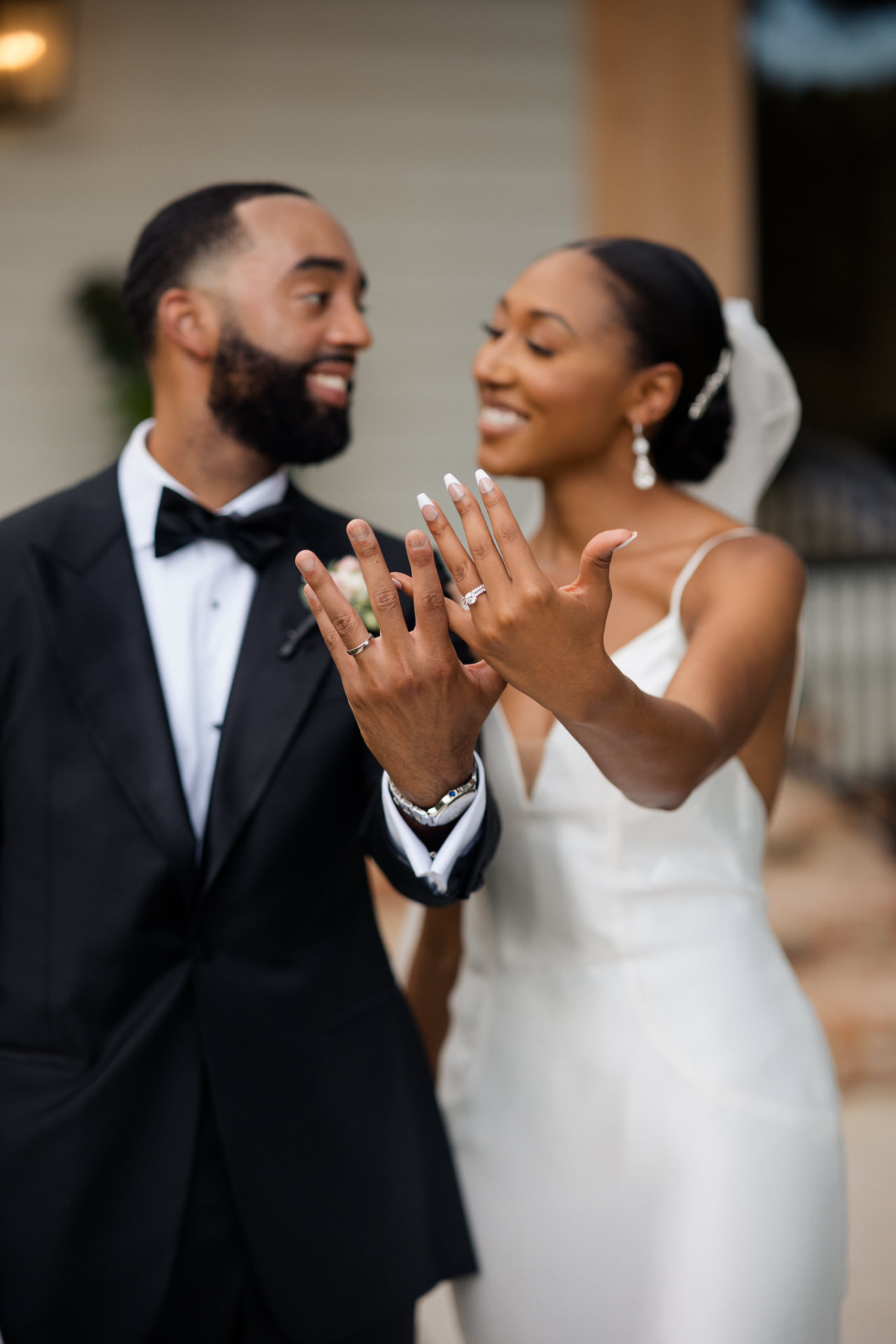 Newlyweds smiling as they show their wedding rings outside the house